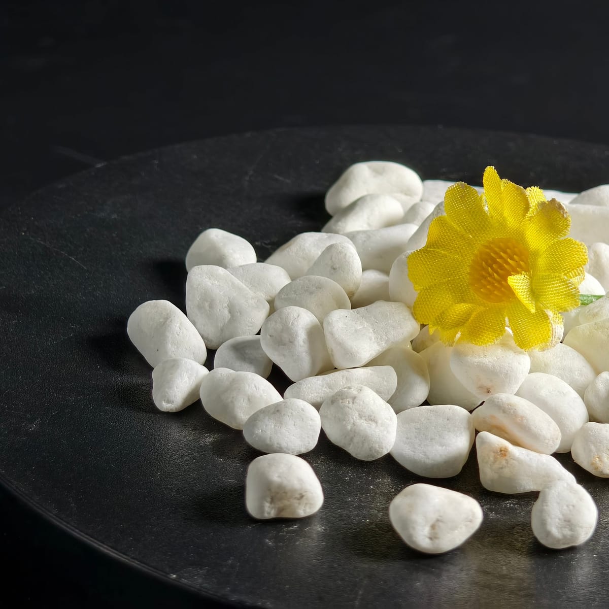 White garden pebbles styled with a yellow flower accent